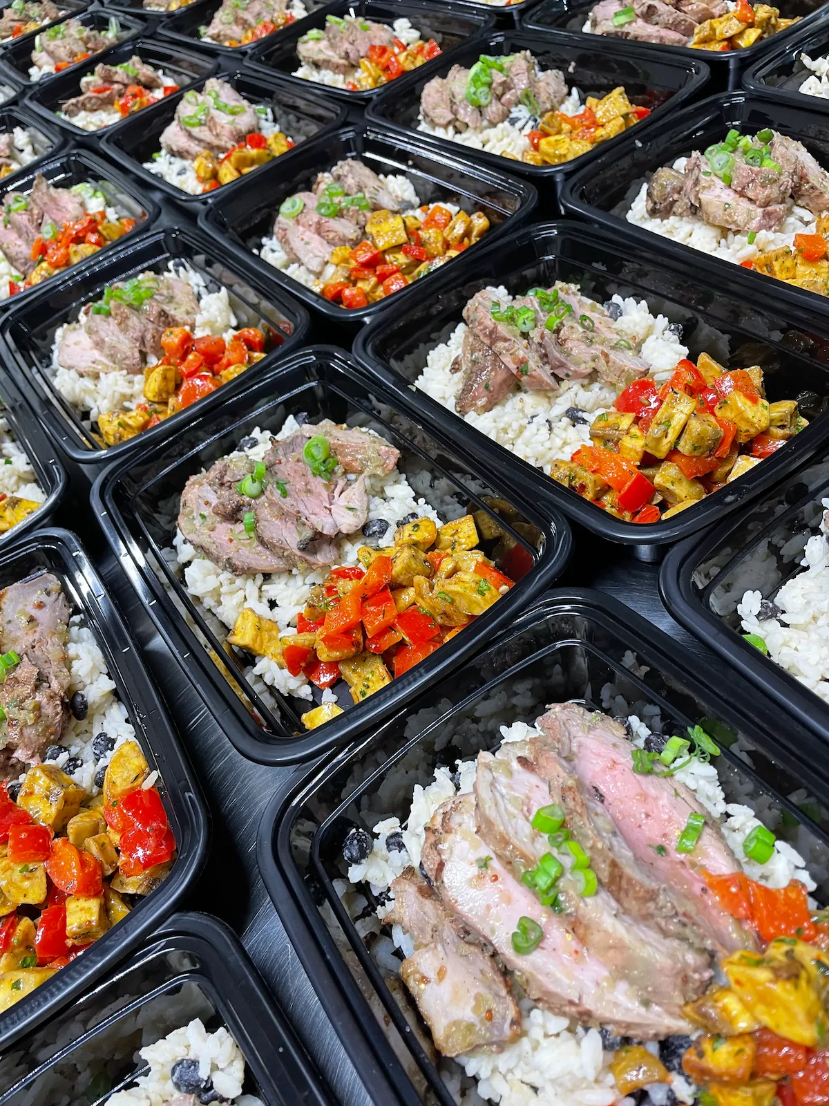 Meal-prep trays with steak, salmon and tofu over rice with black beans and peppers